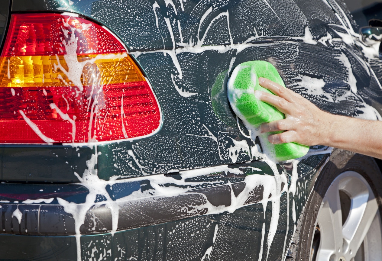 Closeup image of a hand with a soapy sponge washing a vehicle