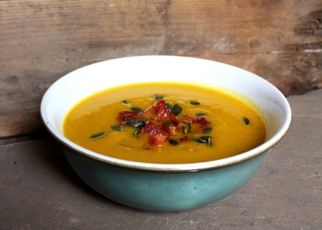 Bowl of pumpkin soup with bacon pieces and pumpkin seed garnish
