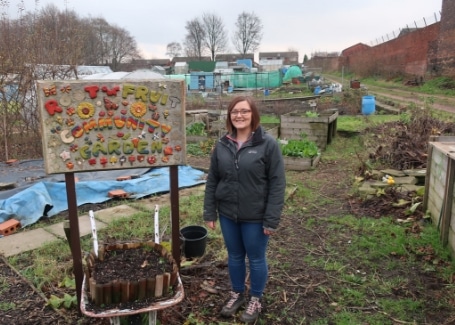 Alex at Root 'n' Fruit's allotment standing next to the Root 'n' Fruit sign