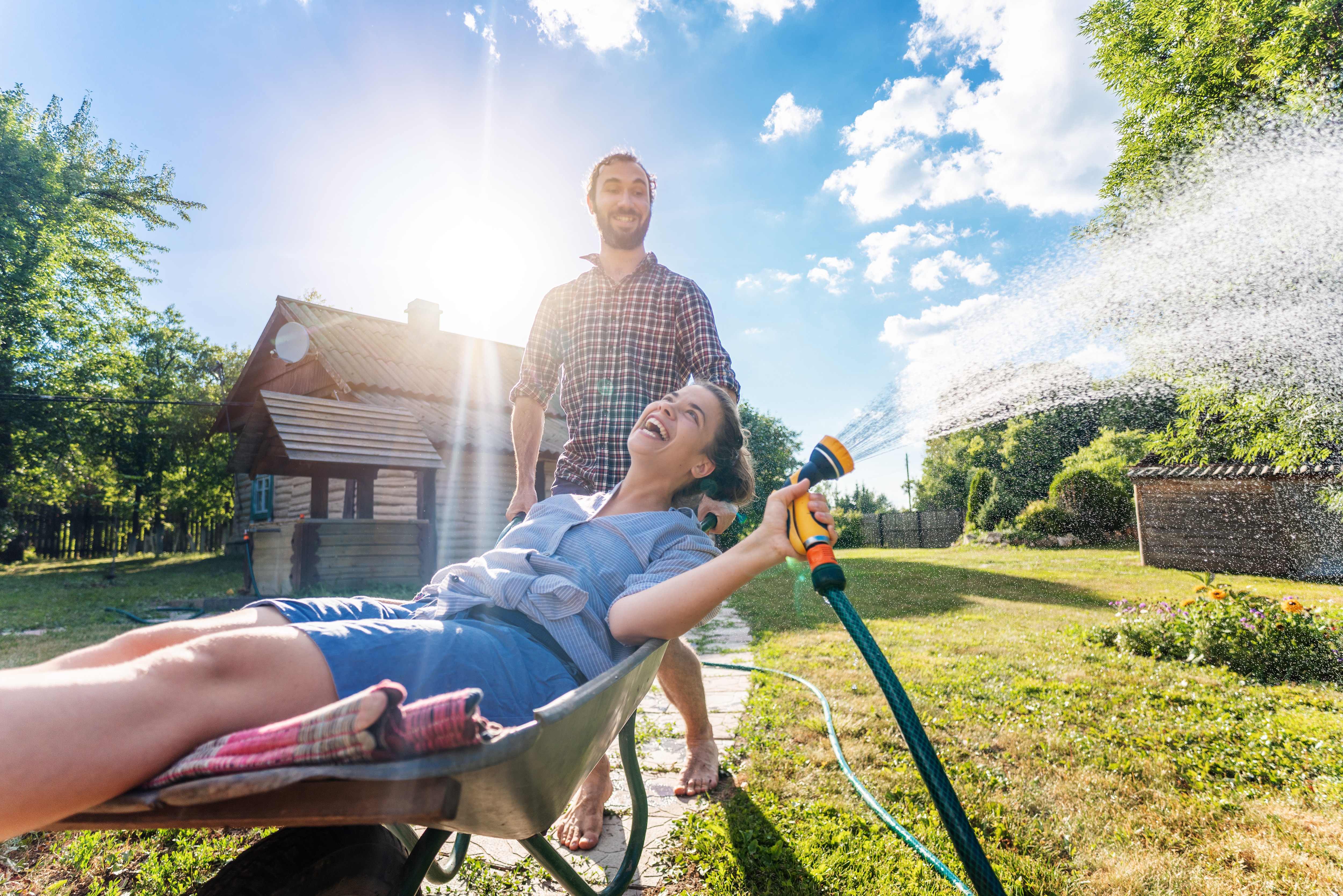 Young happy couple watering garden, a girl with a hose in hand on a trolley, spring and summer concept, eco-friendly lifestyle.