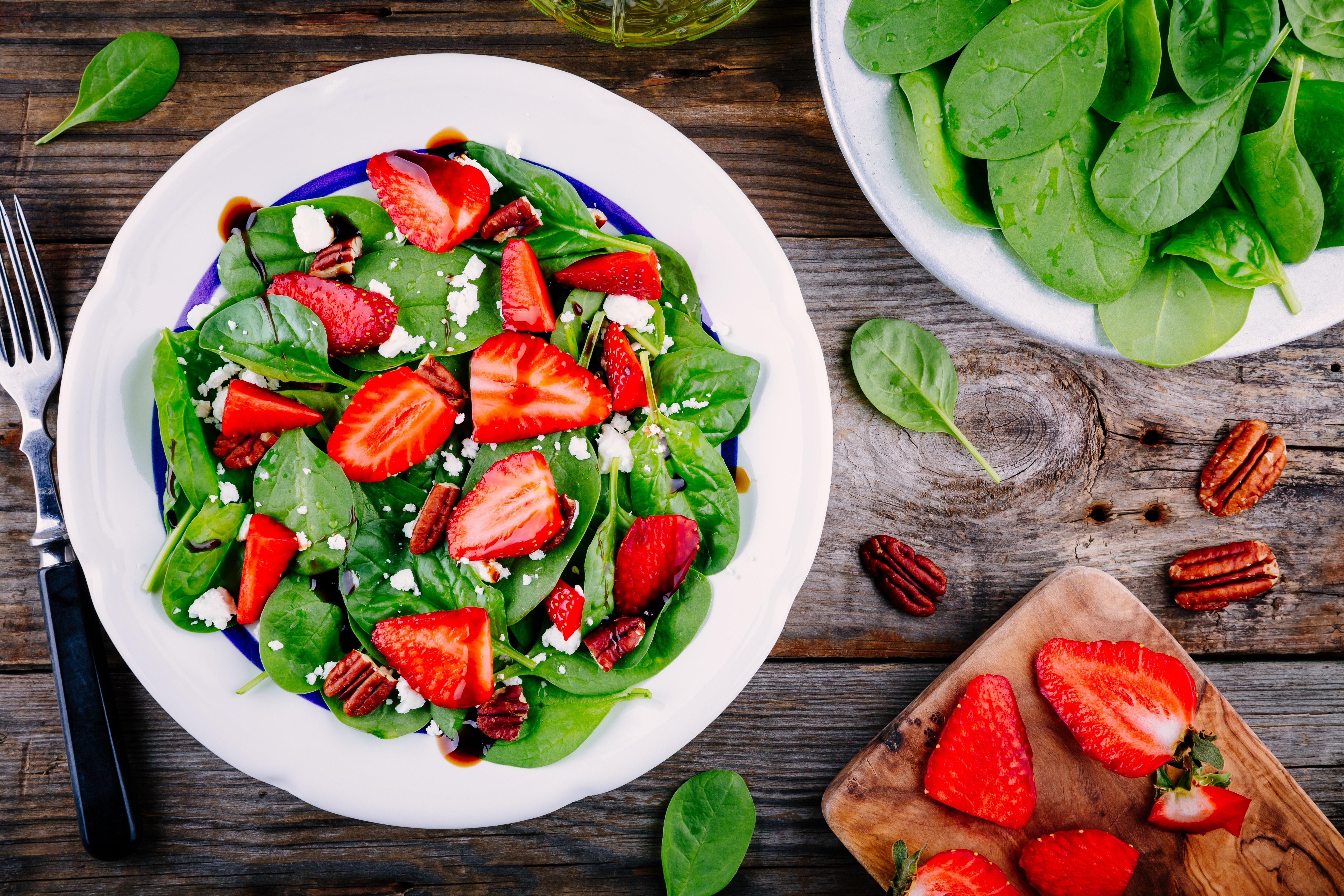 Spinach salad with strawberries, feta cheese, balsamic and pecan nuts on wooden background