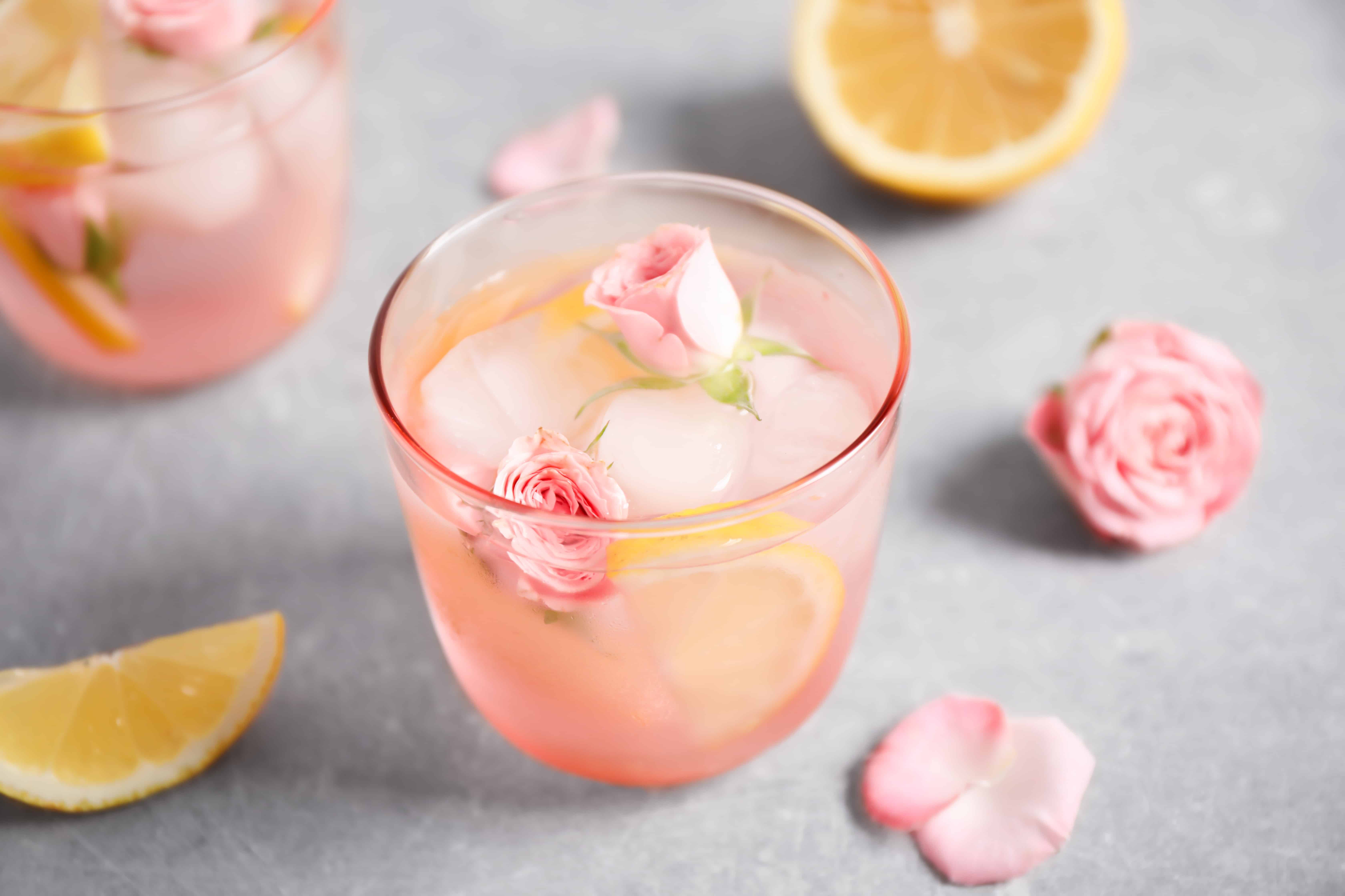 Tasty refreshing lemon drink with roses on light grey table