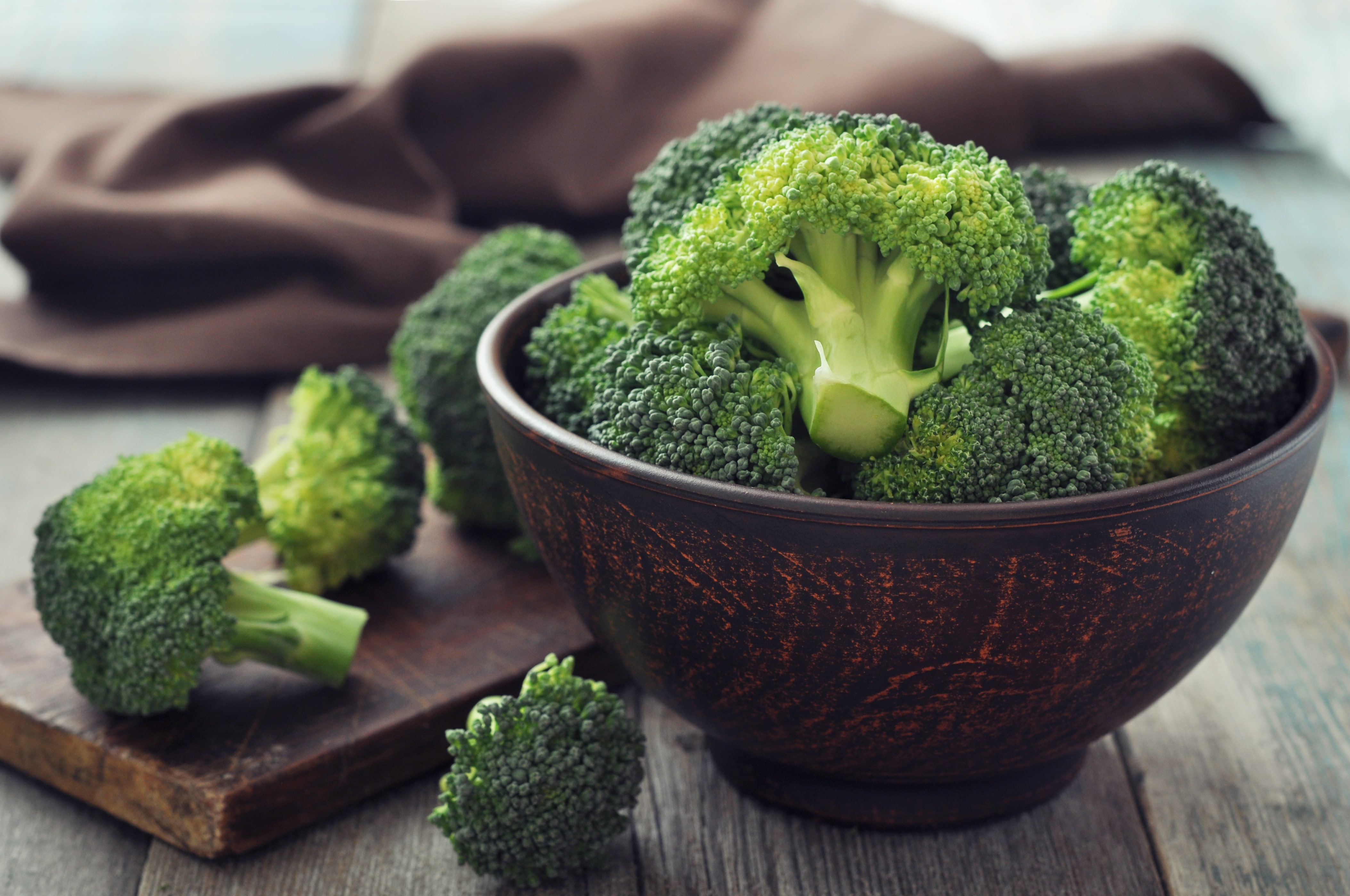 Bunch of fresh green broccoli in brown bowl over wooden background