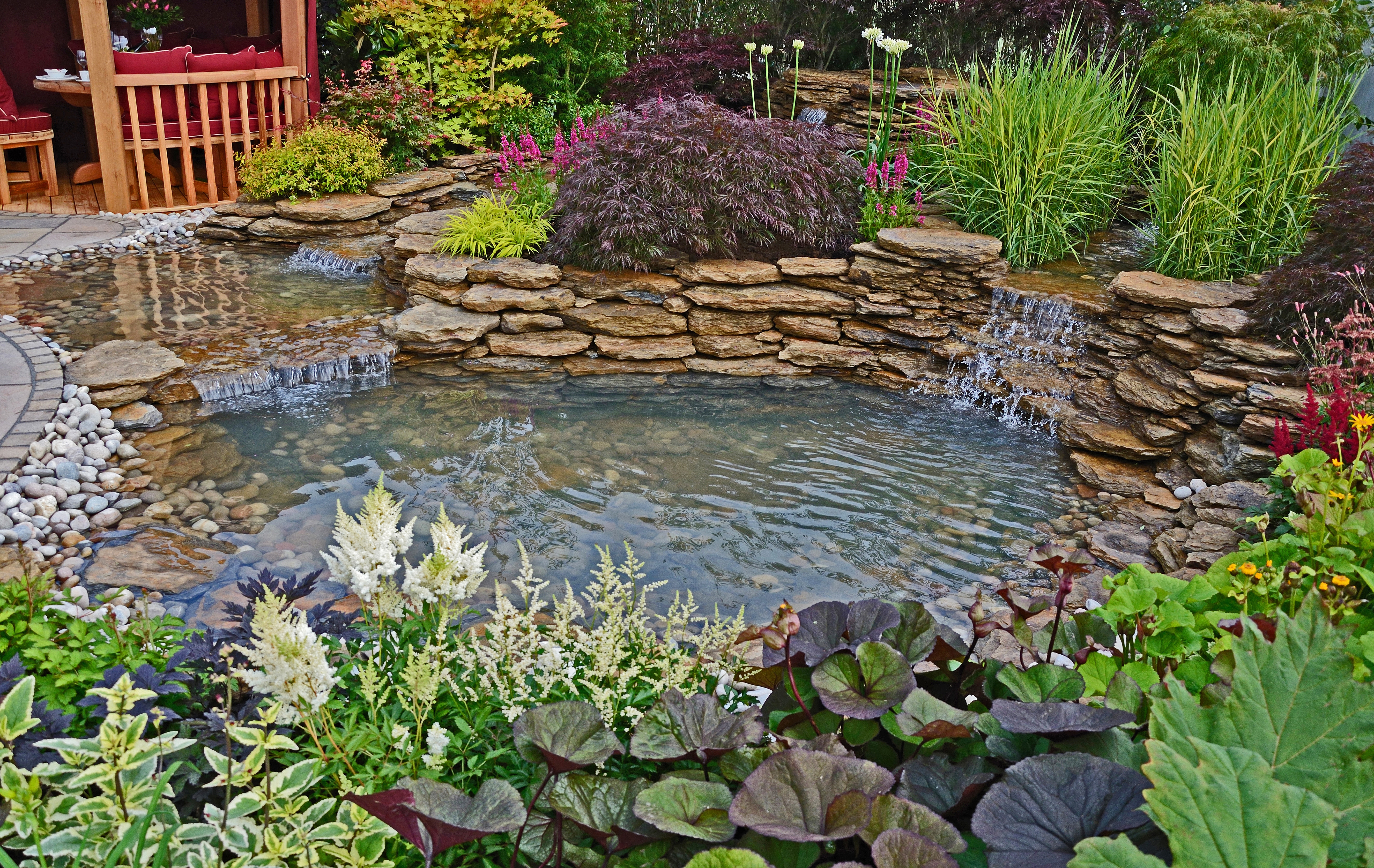 The pond area in an aquatic garden with planted rockery and waterfalls and summer house