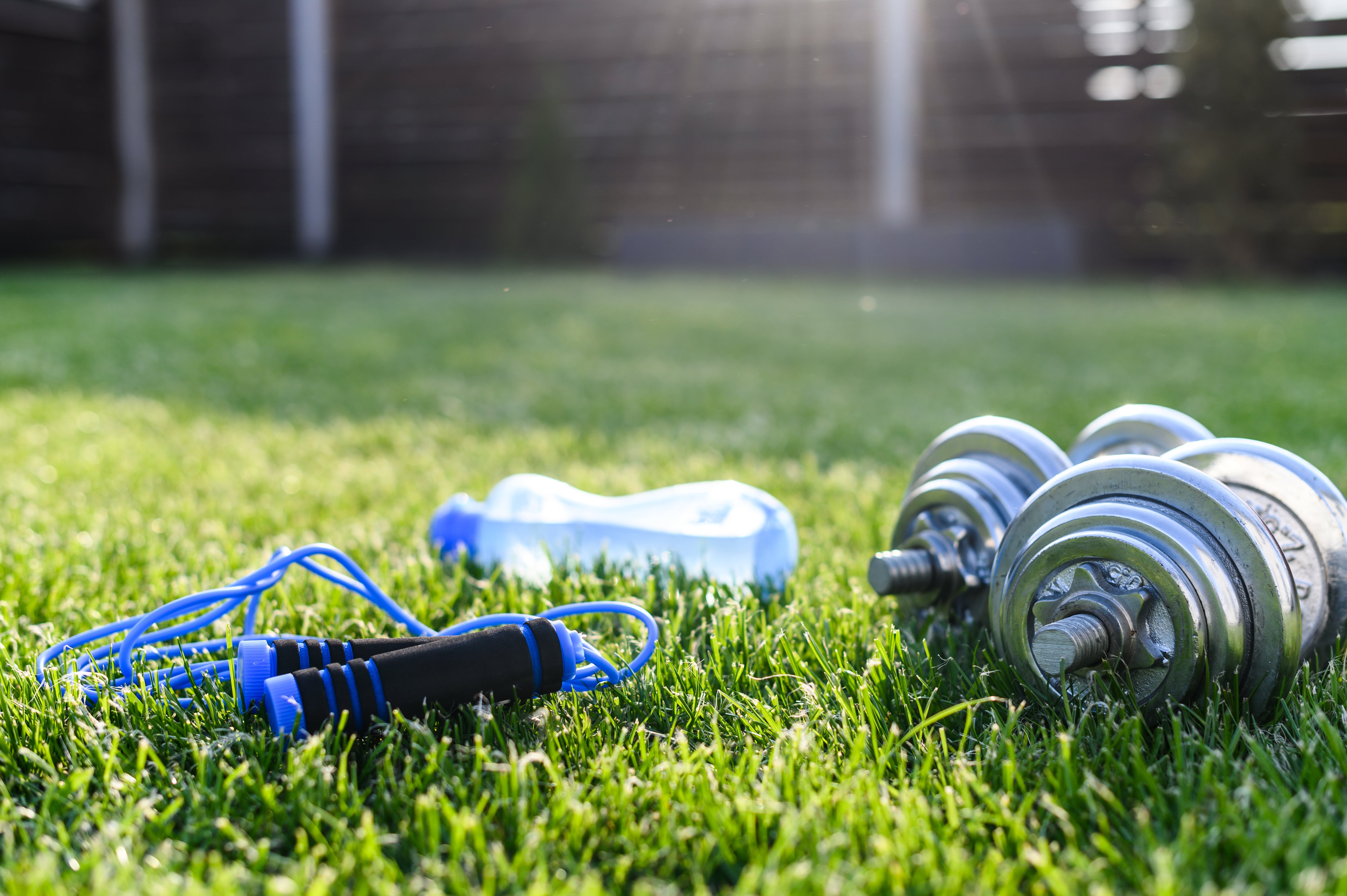 Workout in the backyard. Iron dumbbells, sports bottle of water and jump rope on the greenlawn