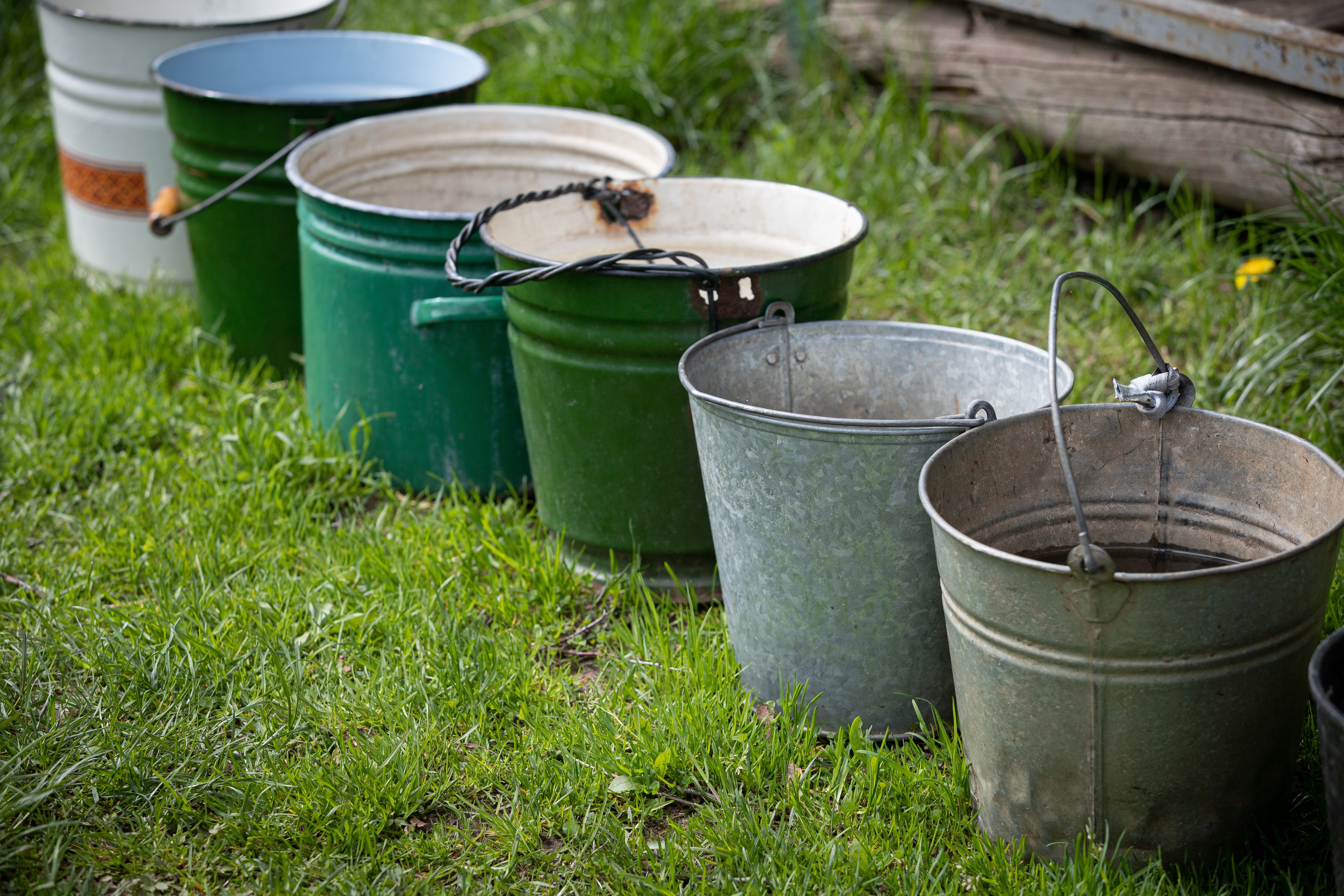 Many different buckets stand in a row to collect rainwater. Buckets of water stand on the grass in the garden next to the house. Village concept